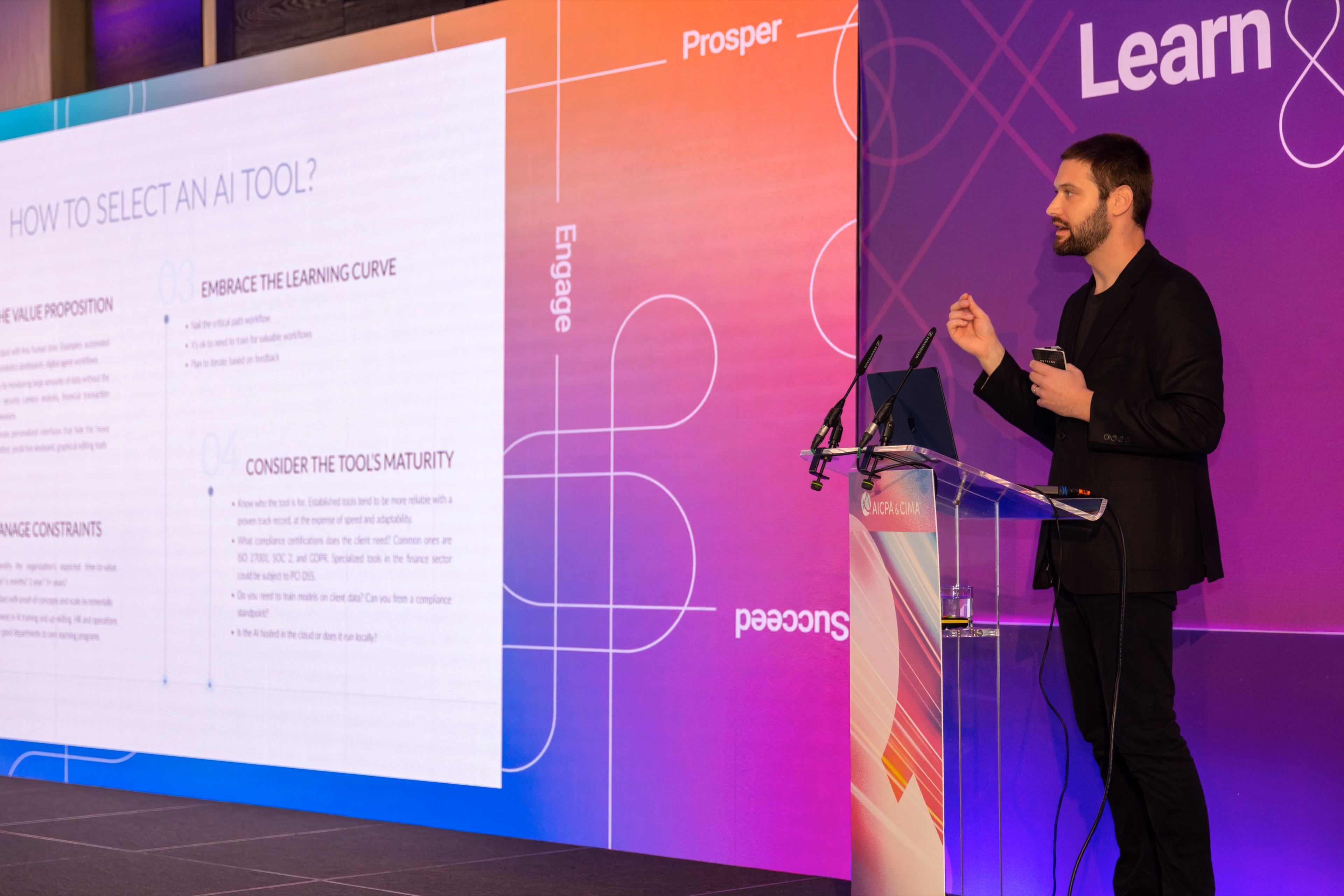 Zach on stage delivering a presentation about selecting AI tools, standing beside a colorful backdrop with a clear podium.