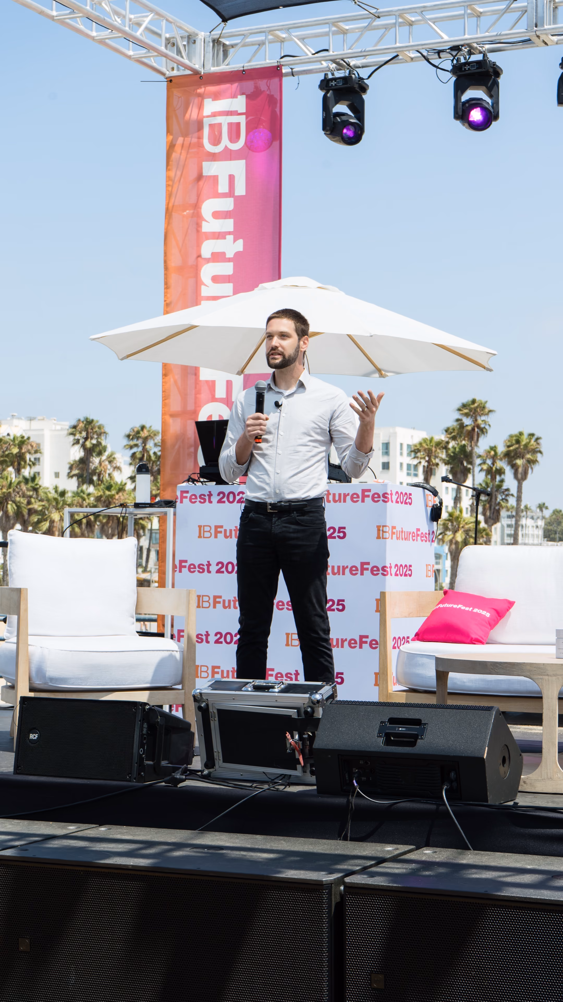 Zach giving a keynote presentation with a microphone on an outdoor stage at FutureFest, surrounded by an audience.