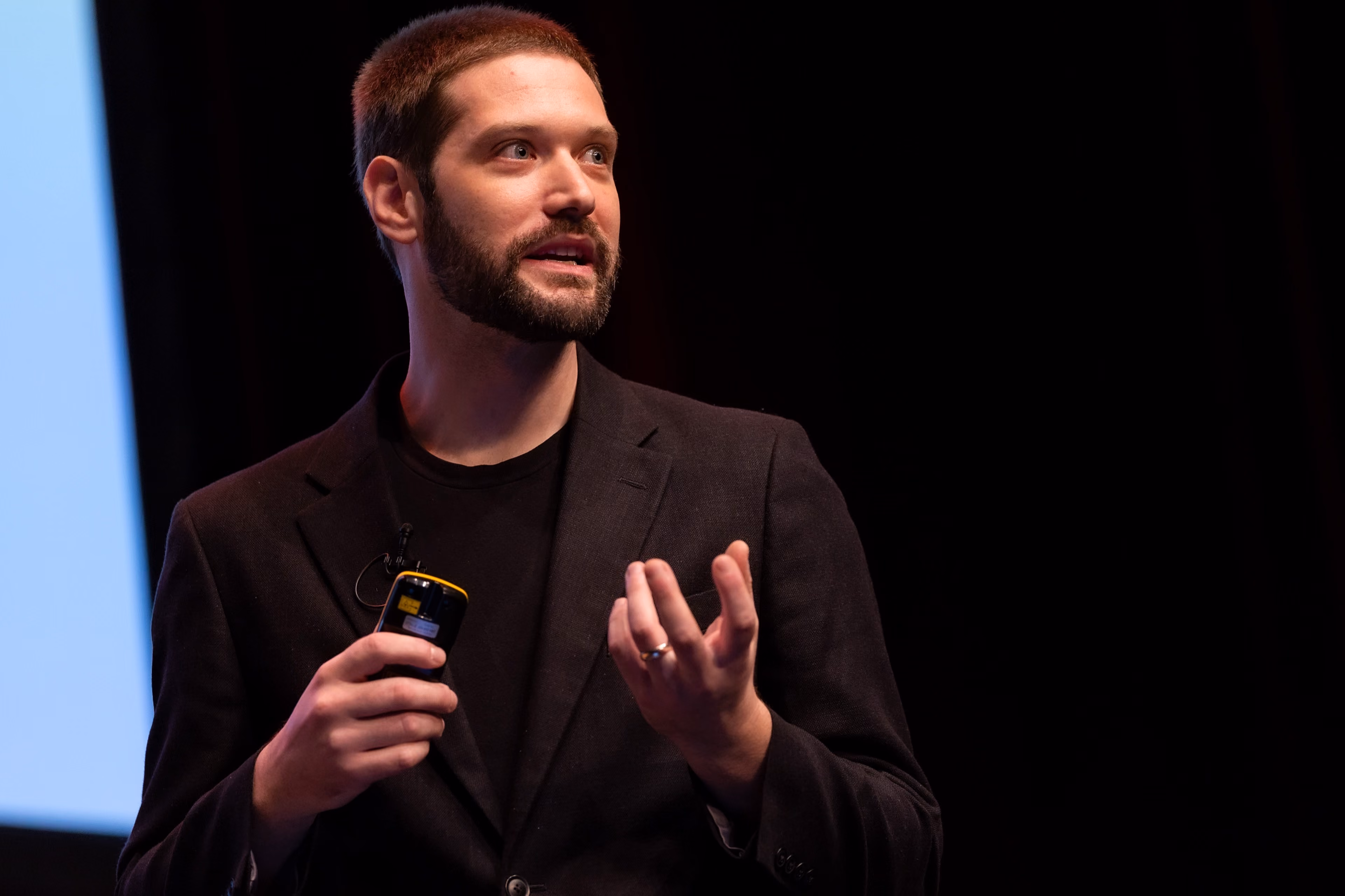 Zach Rattner speaking passionately on stage, holding a clicker.