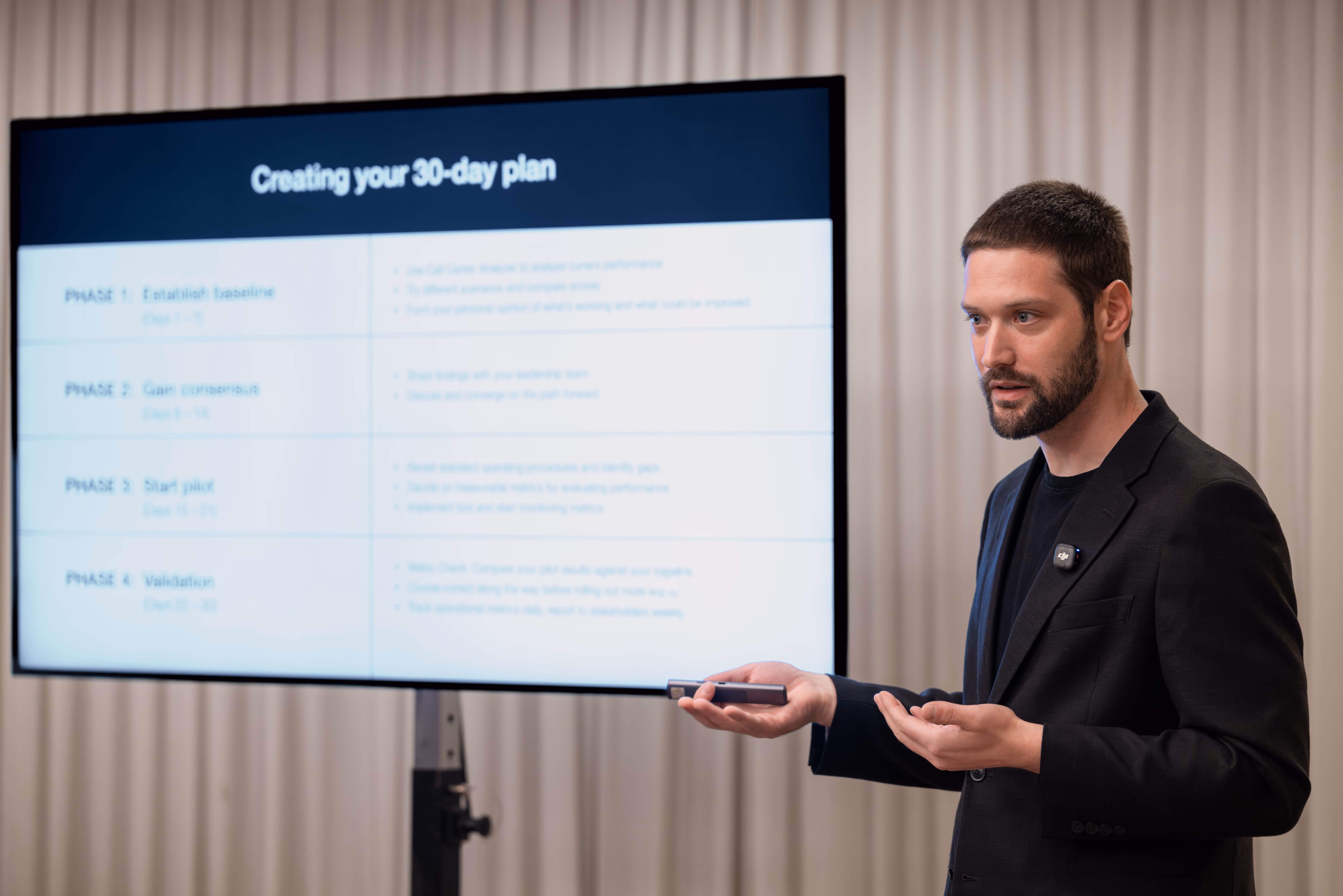 Zach gestures with open hands beside a display showing a slide titled Creating Your 30-Day Plan, which breaks an AI adoption rollout into four phases from baseline to validation.
