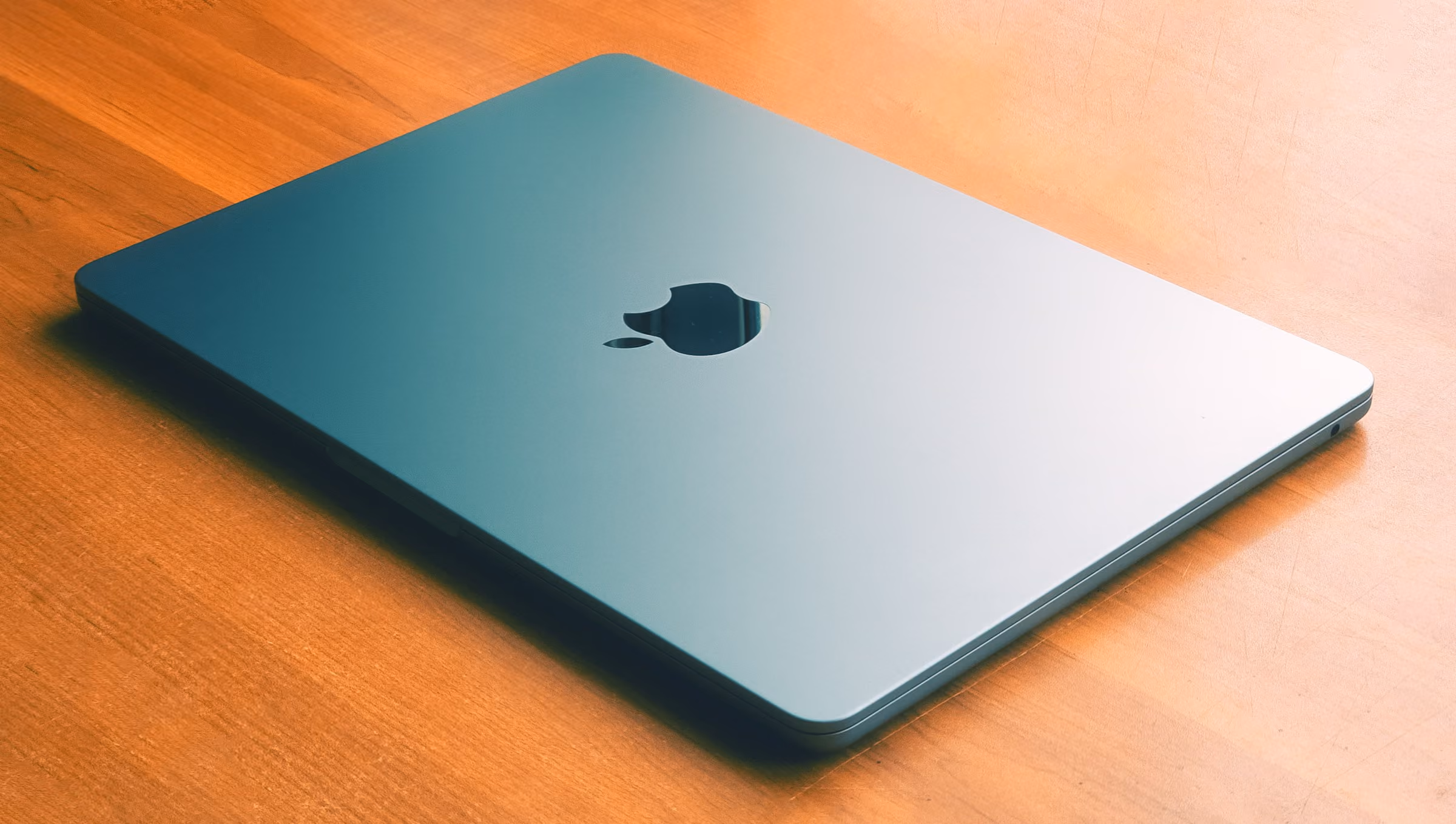 A closed silver MacBook Air on a wooden table, the class of fanless Apple silicon laptop measured here.
